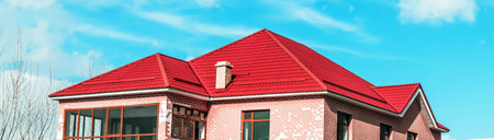 The roof of a cottage with a metal coating, snow guards, a chimney, against the background of a blue sky. Inclined roof of a residential building made of metal profiled sheet, metal slate.の写真素材