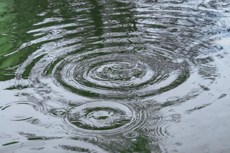 Raindrops over the surface. Bubbles in a rain puddle during a thunderstorm. The smooth surface of a wave of raindrops graduated the shade of the shadow.の写真素材