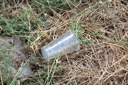 A plastic glass with water on the grass. Garbage from one large empty white plastic cup lies on the ground and in the grass in natureの写真素材