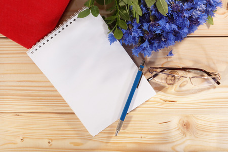 Notebook, pen, spectacles and bouquet of cornflowers on wooden backgroundの写真素材