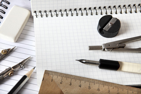 Triangle ruler, compasses, dividers, eraser, a simple pencil and a sharpener lie on a notebook. View...