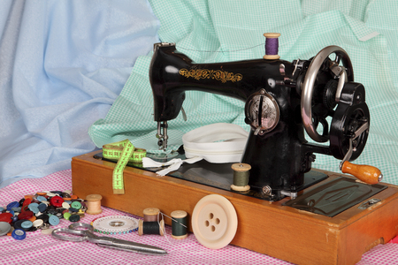 An old, hand sewing machine with a needle, retro coils with colored threads, bright buttons and pieces of colored cotton fabric.の写真素材