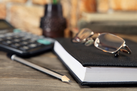 The diary, glasses and a simple black pencil lie on the desktop. Close-up. Selective focusの写真素材
