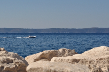 Man in boat on the sea, stones in front, island Hvar in backgroundの写真素材