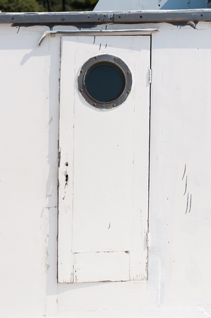 Old white wooden door on the ship with a circular windowの写真素材