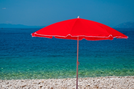 Beach with pebbles and red sunshade with sea in background on a summer dayの写真素材