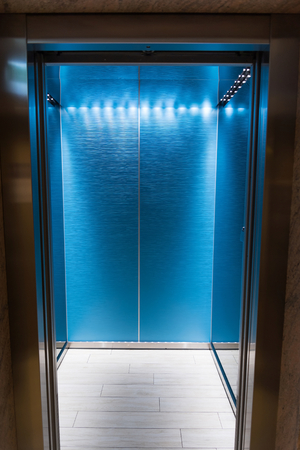 An empty modern blue elevator or lift with metal doors that are open in building with lighting. Vertical photoの写真素材