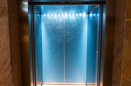 An empty modern blue elevator or lift with metal doors that are open in building with lighting....