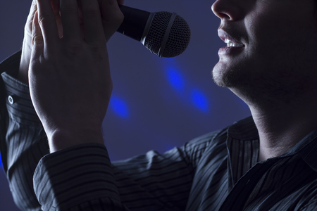 Handsome man singing to microphone with colorful background lights.の写真素材
