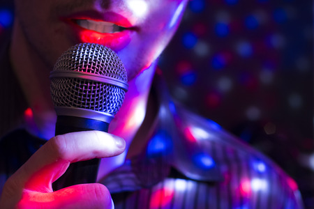 Young man singing with a microphone with colorful background lights.の写真素材