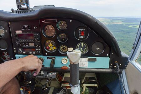 Close up of a man in a cockpit piloting small four seat airplane, pushing buttons on control panel with hills and meadows in distanceの写真素材