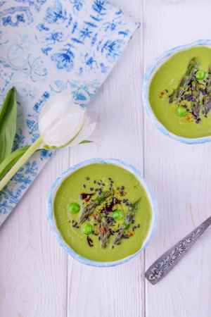 Homemade green cream soup with asparagus and green peas on a white wooden background. Top view, free spaceの写真素材