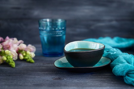 Black coffee in a turquoise cup, a glass of water and snapdragons flowers on a black background.の写真素材