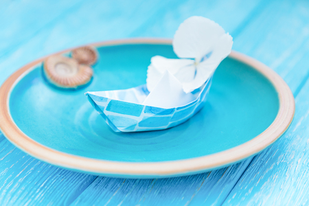 Paper boats with flower in a ceramic bowl on a blue wooden background. Summer traveling concept. Free spaceの写真素材