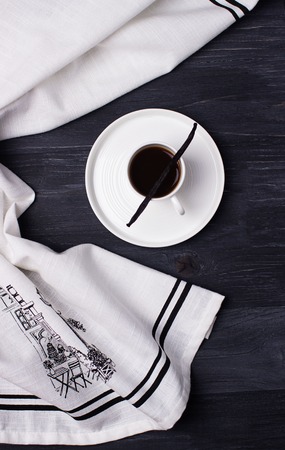 Black coffee in a white cup and vanilla pod on a black wooden background. Black and white colorsの写真素材