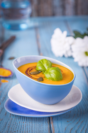Pumpkin cream soup with pumpkin seeds, pumpkin oil and turmeric on a blue backgroundの写真素材