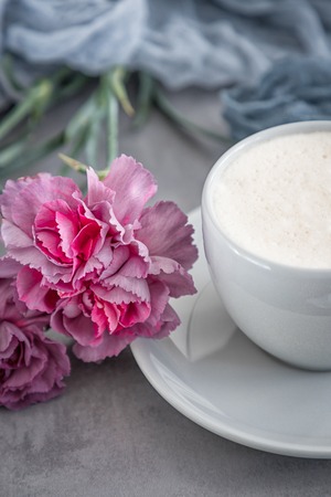 Cup of coffee cappuccino and pink carnation flowers on a gray backgroundの写真素材