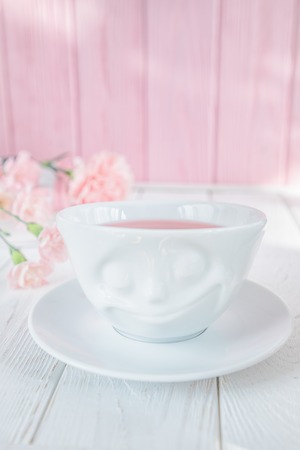 Fruit tea in white cup and pink carnation flowers on a white wooden background. Free spaceの写真素材