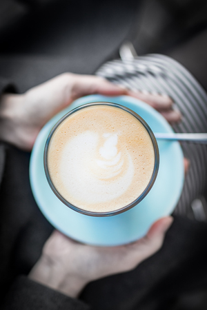 Female hands holding a turquoise cup of coffee latte on a black and white backgroundの写真素材