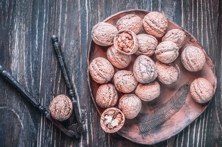 Walnuts in a ceramic plate and old metal nutcracker on a wooden backgroundの写真素材