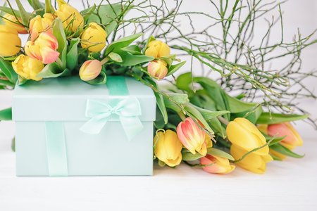 Delicate elegant gift box and a lot of spring yellow tulips on a white background