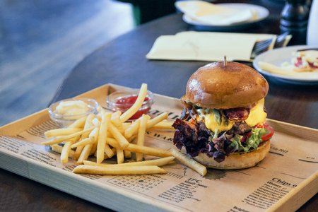 Burger with lettuce and bacon and french fries on the newspaperの写真素材