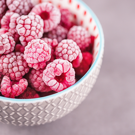 Frozen raspberries in a gray bowl on a gray background. Copy space. Concept fresh berries any time of the yearの写真素材