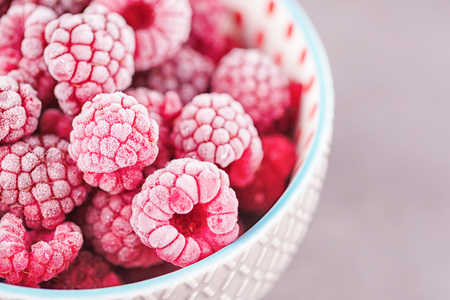 Frozen raspberries in a gray bowl on a gray background. Copy space. Concept fresh berries any time...