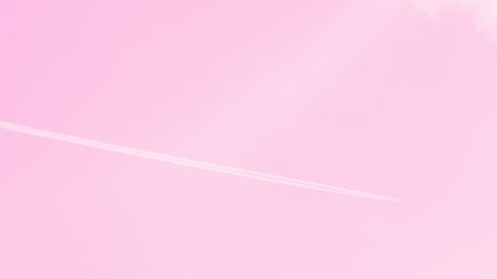 Airplane or flying plane with contrails in a clear light pink sky. 16:9. Copy spaceの写真素材