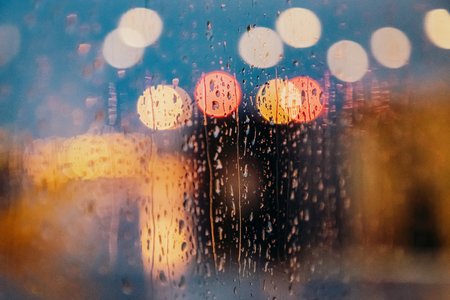 Bright light of evening city and rain drops on the window. Abstract blurred background. Toned photoの写真素材
