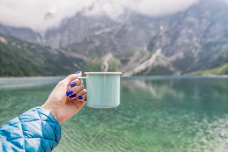 Female hand holding mint color enamel cup.Wonderful nature. Crystal clear lake and mountains. Tatra National park, Poland. Famous lake Morskie Oko or Sea Eyeの写真素材