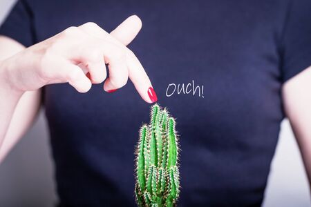 Female hand with red nail polish and green cactus. Ouch. Prickly prick. Black background