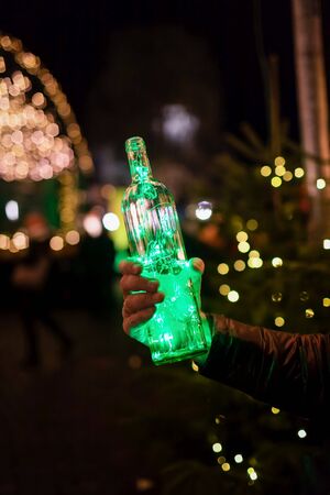 Magic Christmas. Green garland in the bottle on the festive evening city background. Garland in the hand, toned photo. Copy spaceの写真素材