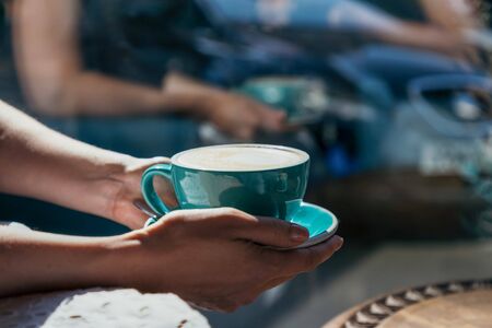Female hands holding a green cup of coffee cappuccino. Light and shadowの写真素材