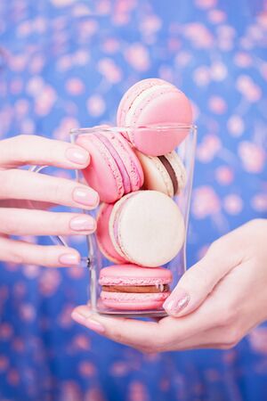Beautiful female hands holding transparent cup with pink and beige macaroons. Manicure with pink color nail polish. Natural manicure with sparklesの写真素材