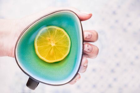 Female hand holding a turquoise cup of lemon tea. Top view, copy spaceの写真素材