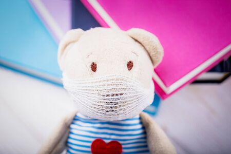 Cute toy teddy bear in a medical mask on a colored books background. Home occupation conceptの写真素材