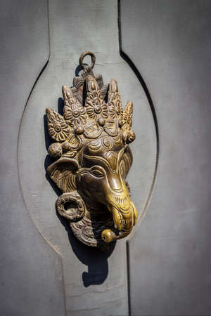 Hindu God Ganesha. Vintage metal door knocker on an gray wooden door, verticalの写真素材