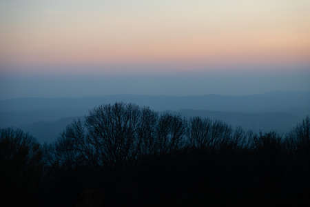 Layered mountains, trees silhouette. Smokey blue mountain silhouettes background, pastel evening sky. Trees silhouetteの写真素材