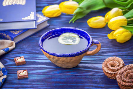 Ceramic cup of lemon tea, yellow tulips and books and chocolate pieces with an Easter bunnyの写真素材