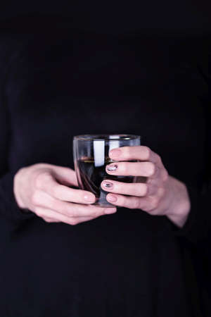 Female hands holding transparent glass cup of black coffee. Manicure with pink color nail polish, black floral patternの写真素材