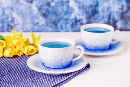 Two cups of exquisite blue tea and bouquet of daffodils, trendy blue butterfly teaの写真素材