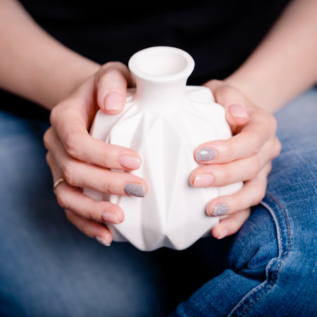 Female hands holding white ceramic vase. Manicure with pink and gray color nail polish, square photoの写真素材