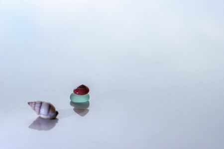 Minimalism. On a light background with reflections there is a green glass and a red shell with a pyramid, and another shell is next to it. Selective focus. Place for text.の写真素材