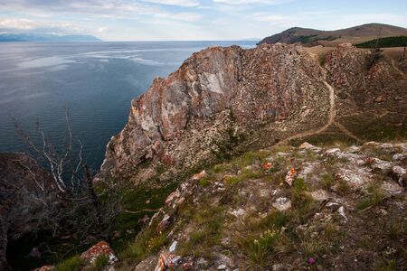 A large rock on the shore of Lake Baikal. There is a path to the rock. There is a dry tree. Behind a mountain lake in haze.の写真素材