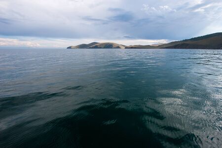 Beautiful view of the water of Lake Baikal per day with clouds in the sky. View from the water. The water is green. On the horizon are hills.の写真素材