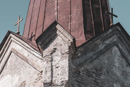 Rusty roof of a church with two crosses. Ancient historical building. Old stones. Cracked plaster.