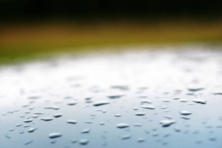 Background with blurred drops on the roof of a silver blue car and a green backdrop. Slight gradient above the roof. There is a place for text. Soft focus. Selective focus.の写真素材
