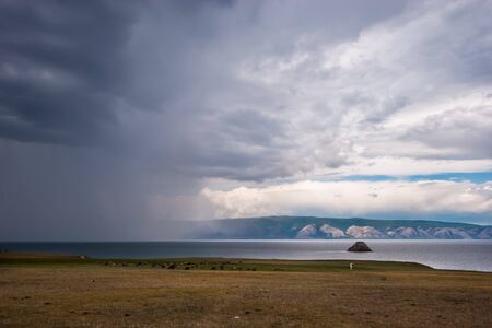 Rain over Lake Baikal and the cows on the shore on a cloudy day. Over the rain and the lake you can...