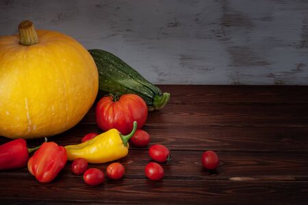 Still life of pumpkin, zucchini, tomatoes and peppers on the boards. The boards are brown, the background is carelessly painted with white paint. Vignette.の写真素材